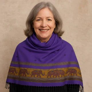 Femme âgée souriante, châle violet à franges et motifs éléphants dorés, fond neutre beige.