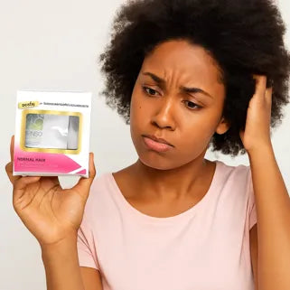 Mujer afro perpleja mirando un producto capilar, se rasca la cabeza con preocupación.