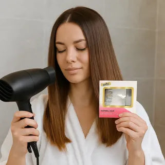 Femme en peignoir utilisant un sèche-cheveux avec un produit capillaire pour cheveux normaux.