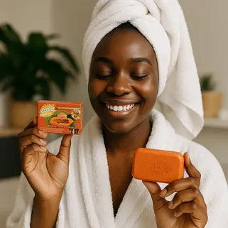 Mujer sonriente en bata muestra un jabón aclarador de papaya para piel negra.