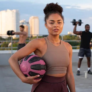 Femme sportive tenant un ballon rose, entraînement en plein air avec haltères.