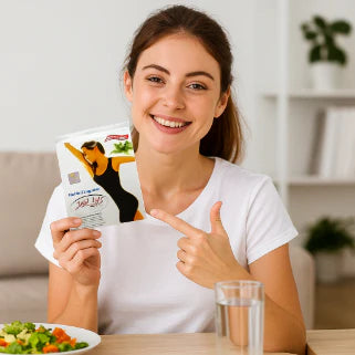 Femme souriante à table pointant un sachet de produit minceur à côté d'une salade.