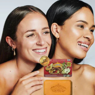 Deux femmes souriantes présentent un savon éclaircissant tamarin, gingembre et miel, reflétant un teint radieux.