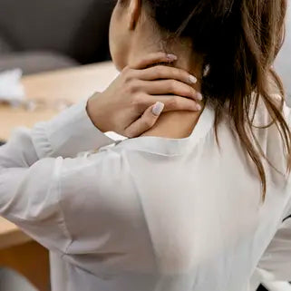 Femme au bureau souffrant de douleurs cervicales, se masse la nuque pour soulager la tension.
