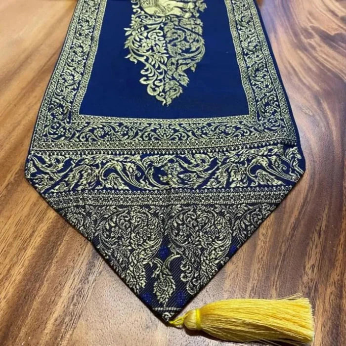 Del av en bordslöpare i koppartyg med guld tofsar. Duk presenterad på ett träbord.