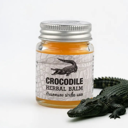 Petit pot de Crocodile Herbal Balm posé à côté d’un crocodile décoratif. Baume à base d’herbes utilisé pour apaiser vite irritations, petites blessures et inconforts cutanés. Packaging avec illustration de crocodile, évoquant un soin puissant et protecteur.