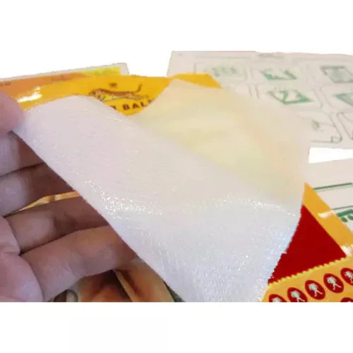 Main tenant un morceau de papier bulle partiellement décollé, révélant un paquet jaune et rouge en dessous. En arrière-plan, des feuilles avec des illustrations vertes.