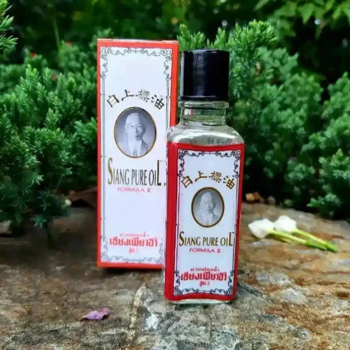 bouteille avec son emballage de Siang Pure Oil Formule II Blanche sur un rocher avec des arbres en fond.