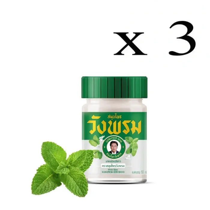 Trois Pots de baume blanc Wangprom Herb avec couvercle vert, étiquette verte en thaï et anglais avec des feuilles de menthe, et feuilles de menthe en premier plant