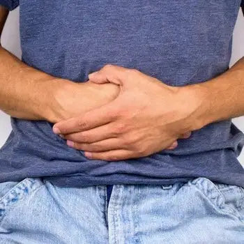 Personne en t-shirt bleu, mains sur l'abdomen exprimant une douleur intense