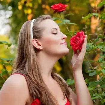 Une femme blonde sentant une rose rouge dans un jardin fleuri