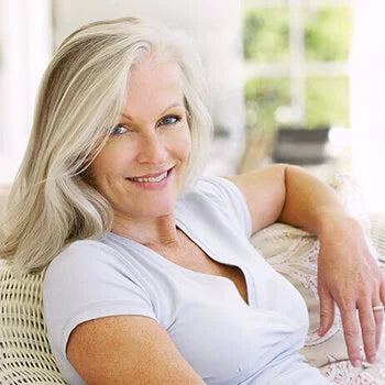 Femme blonde souriante, cheveux longs, t-shirt blanc, intérieur lumineux.