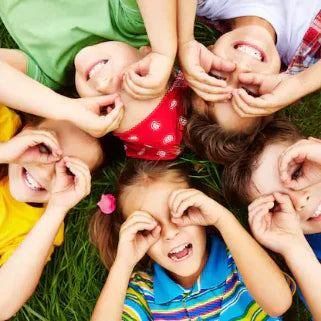 Enfants souriants jouant dans l'herbe, formant des lunettes avec leurs mains pour s’amuser.