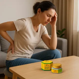 Femme souffrant du dos assise avec un baume de massage posé sur une table basse.