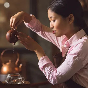 Femme en rose versant du thé d'une théière traditionnelle chinoise.