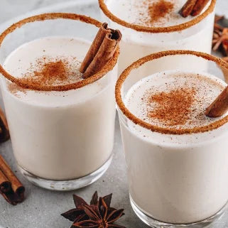 Trois verres de boisson à la cannelle, garnis de bâtons de cannelle et poudre parfumée.