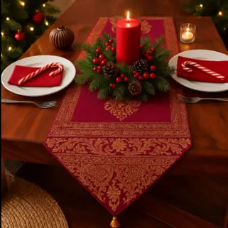Chemin de table rouge et or avec bougie, décorations de Noël et couverts élégants.