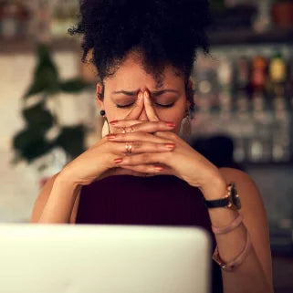 Une femme assise à un bureau, les mains sur le visage, illustrant le stress et l'anxiété, nécessitant des clous de girofle 