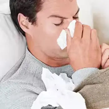 Homme malade au lit, mouchant son nez avec un mouchoir.