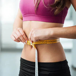 Une Femme portant une brassière de sport rose et un pantalon de sport noir, mesurant son tour de taille avec un mètre ruban