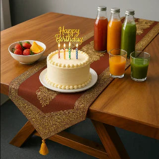 Table décorée avec gâteau d'anniversaire, bougies, jus colorés et chemin de table rouge.