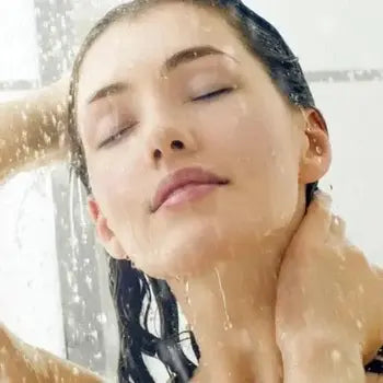 Femme sous la douche, yeux fermés, visage levé, eau ruisselante.