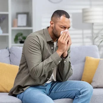 Un homme assis sur un canapé se couvrant le nez et la bouche