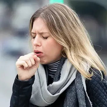 Femme toussant à l'extérieur ayant des symptômes de la toux, potentiellement liée à un rhume.