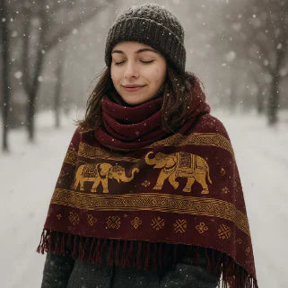 Femme souriante yeux fermés, bonnet gris, châle bordeaux à motifs éléphants dorés, flocons de neige.