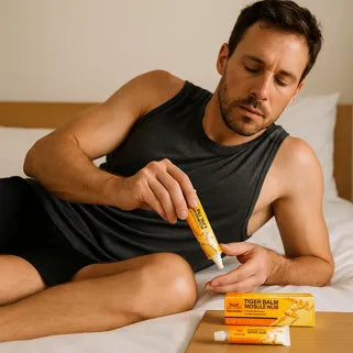 Homme appliquant la Pommade Spéciale Muscles Baume du Tigre® sur son bras dans une chambre. 