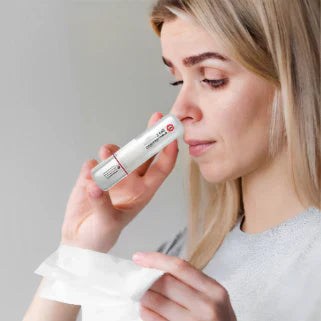 Femme blonde tenant un inhalateur nasal Siang Pure menthol-eucalyptus, soulageant la congestion nasale avec mouchoir