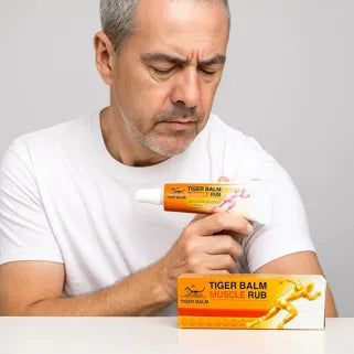 Homme observant un tube de Baume du Tigre Muscle Rub, crème apaisante contre douleurs musculaires.