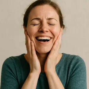 Une femme souriante de bonheur, les yeux fermés, posant délicatement ses mains sur ses joues.
