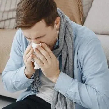 Homme malade se mouchant, portant écharpe et pull bleu clair