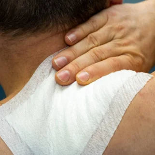 Une main applique un massage thérapeutique sur une épaule recouverte d'un bandage blanc.