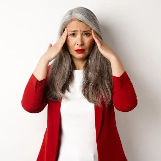 Une femme âgée porte un cardigan rouge, le front plissé avec inquiétude.