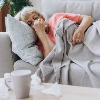 Femme âgée allongée sur un canapé, se mouchant, tasse sur table basse