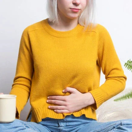 Femme en pull jaune ayant des douleurs à l'estomac assise