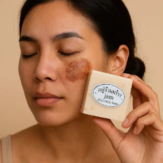 Jeune femme souriante touche sa peau éclatante, tenant le Savon au Lait de Riz.