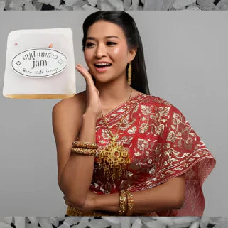 Femme en robe traditionnelle rouge exhibant un savon Rice Milk Soap devant grains de riz
