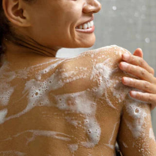 Femme souriante sous la douche, se lavant le dos avec un savon moussant aux bulles abondantes.