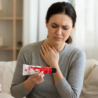 Une femme, l'air souffrant, est assise sur un canapé et tient un tube de pommade.