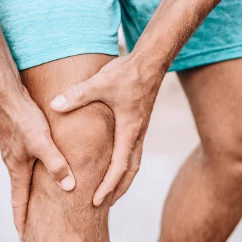 Des mains agrippent un genou douloureux en short bleu clair