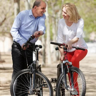 Un homme et une femme souriant, discutant tout en poussant leurs vélos dans un parc ensoleillé