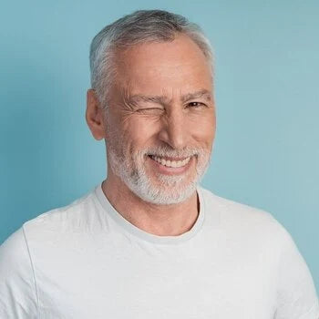 Homme âgé souriant avec barbe grise sur fond bleu clair