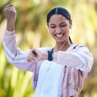 Femme énergique souriante regardant sa montre après l'entraînement, écouteurs dans les oreilles