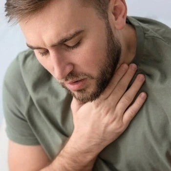 Homme barbu en t-shirt vert touchant sa gorge avec une expression inconfortable.