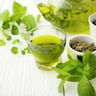 Tasse de thé vert avec des feuilles fraîches et séchées, théière en arrière-plan.