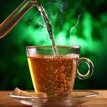 Taza de vidrio transparente recibiendo agua caliente humeante, con fondo verde y cubos de azúcar.