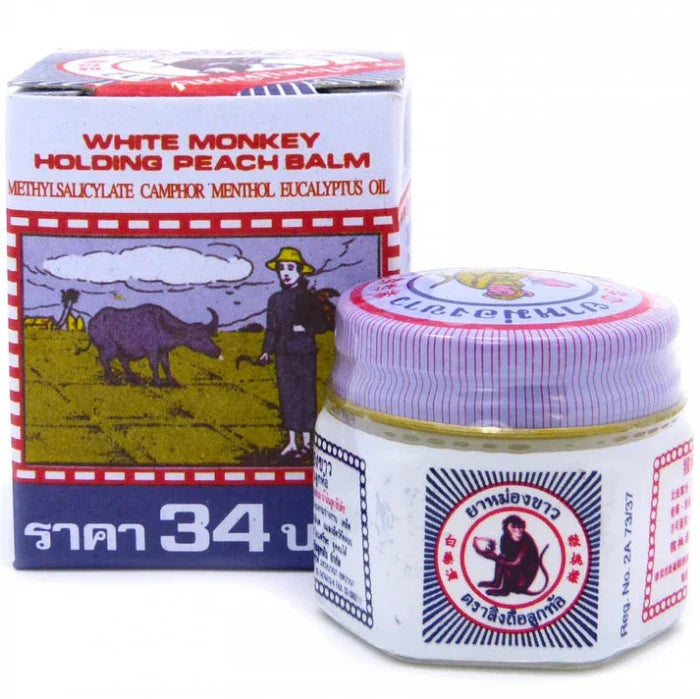 Produit appelé 'White Monkey Holding Peach Balm' avec un pot en verre et son emballage en carton. L'étiquette indique les ingrédients : Methylsalicylate, Camphre, Menthol, Huile d'Eucalyptus. Une illustration sur la boîte montre une personne avec un buffle dans un champ.